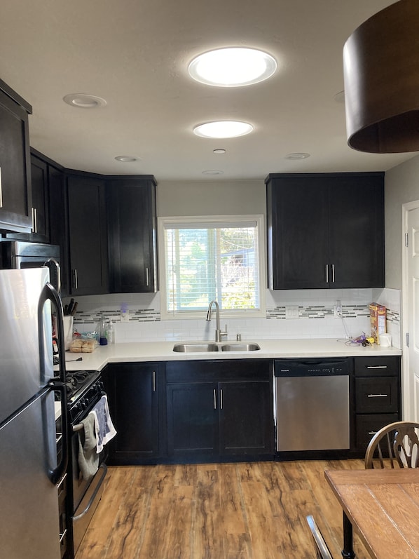 A modern kitchen with dark cabinetry, a stainless steel refrigerator, a dishwasher, and a wooden dining table. - Dog Friendly, Allergen-free 5 minute walk to the bay and eateries (Los Osos -Baywood Park)