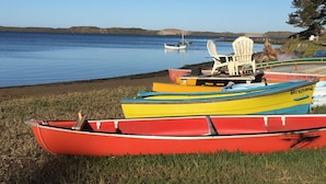 A row of colorful canoes on a grassy shore by a calm lake with boats in the background. - Dog Friendly, Allergen-free 5 minute walk to the bay and eateries (Los Osos -Baywood Park)