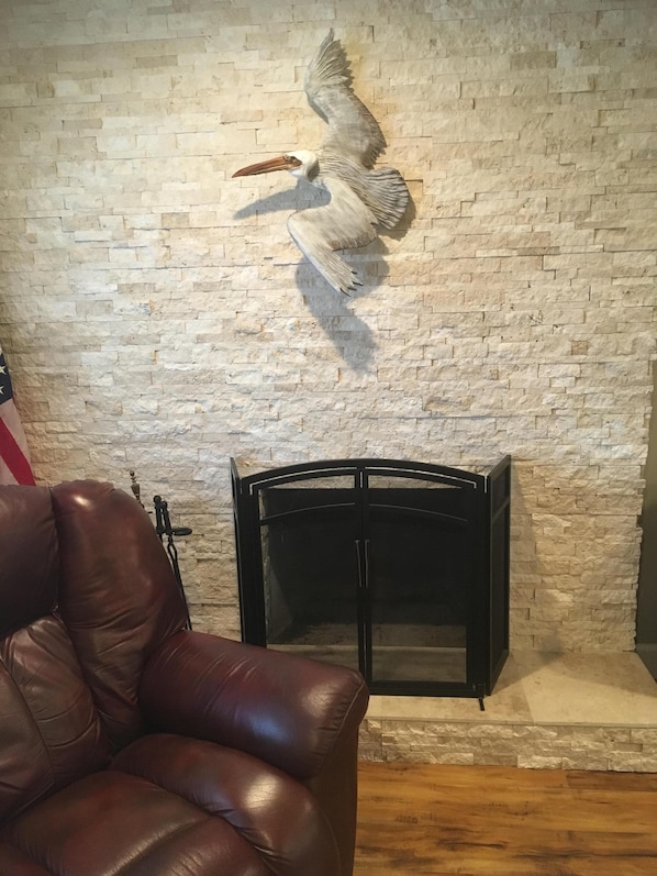 A room with a stone wall, a fireplace, a leather chair, and a mounted bird sculpture.