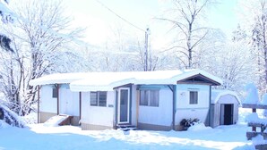 A small, single-story house with a snow-covered roof and exterior. It has a front door, a small porch, and a visible garage door. - Cascade Mountain Getaway (Rockport)