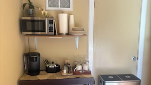 A compact kitchen with a refrigerator, microwave, coffee maker, and a small trash bin.