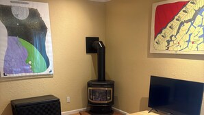 A living room with a wood-burning stove, a television on a wooden cart, a sofa, and a table with a book.