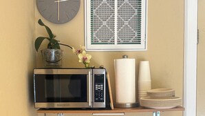 A kitchenette with a microwave, coffee maker, and tea kettle on a wooden counter.