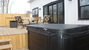 Een terras buiten met een jacuzzi, houten meubels en een wit gebouw met grote ramen.