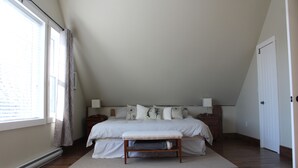 Een slaapkamer met een groot bed, een bankje, een nachtkastje en een bedtafel.