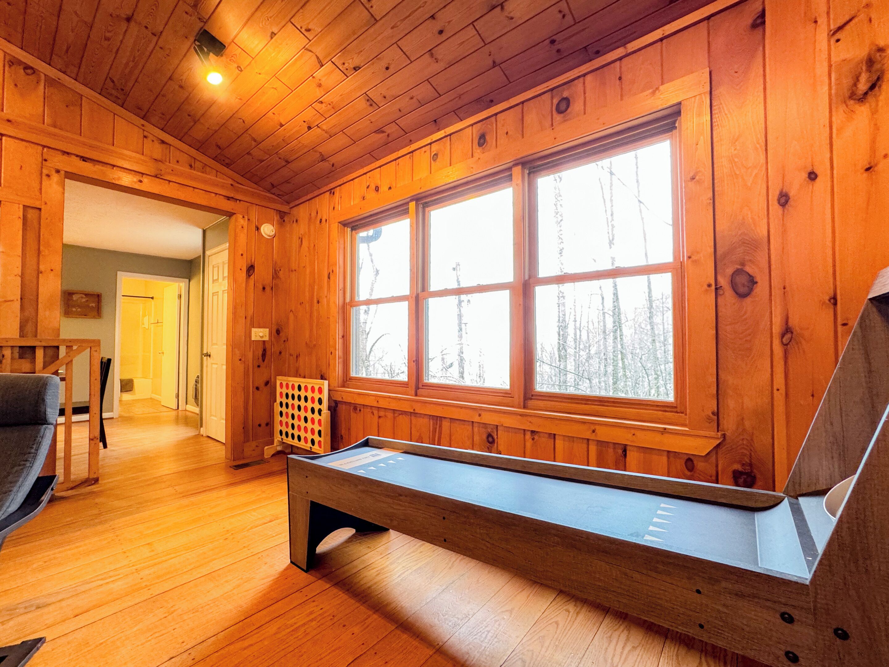 A wooden cabin interior with a large window, a bench, and a door leading to another room.