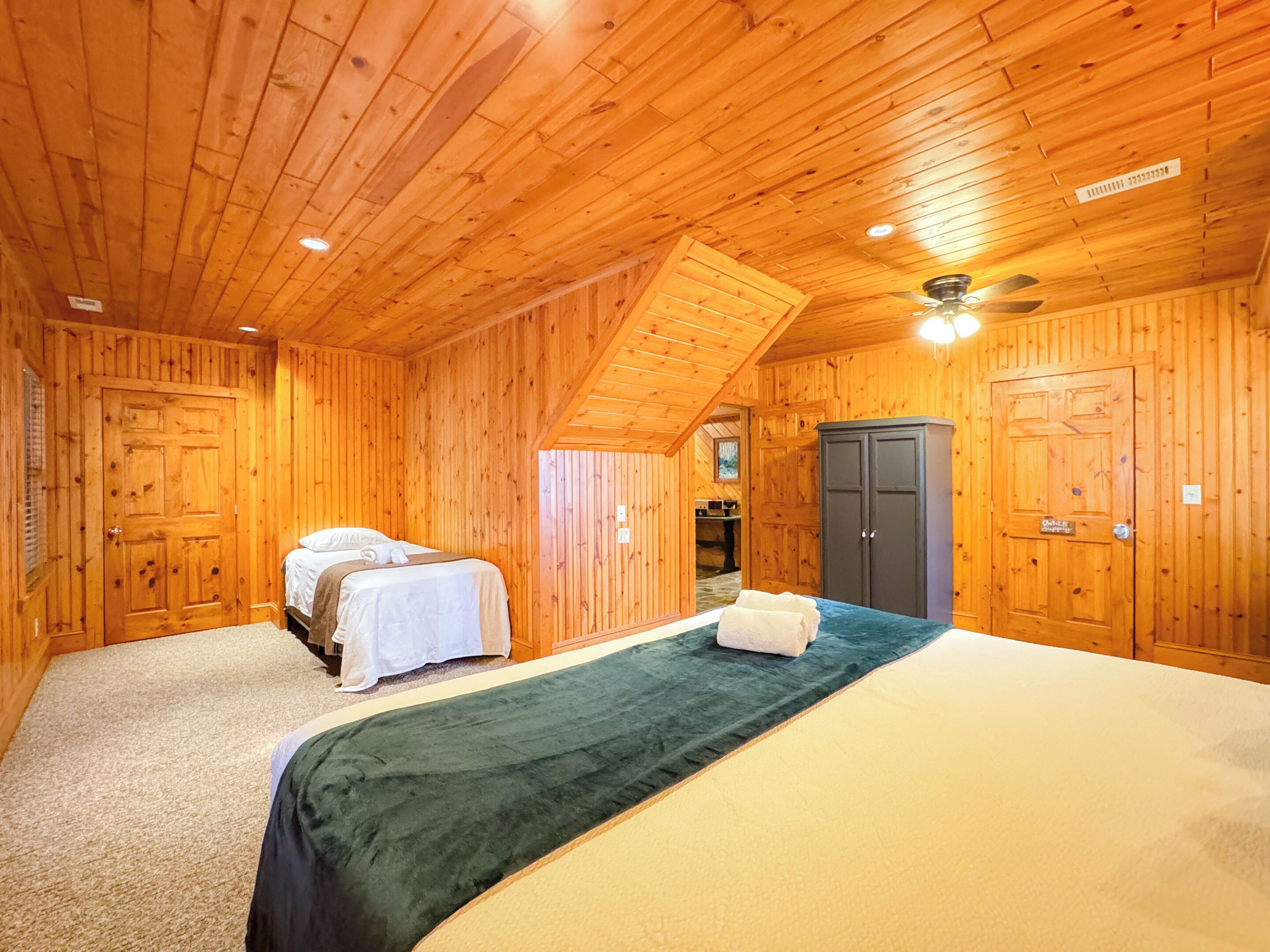 A wooden cabin room with two beds, a wardrobe, and a ceiling fan.