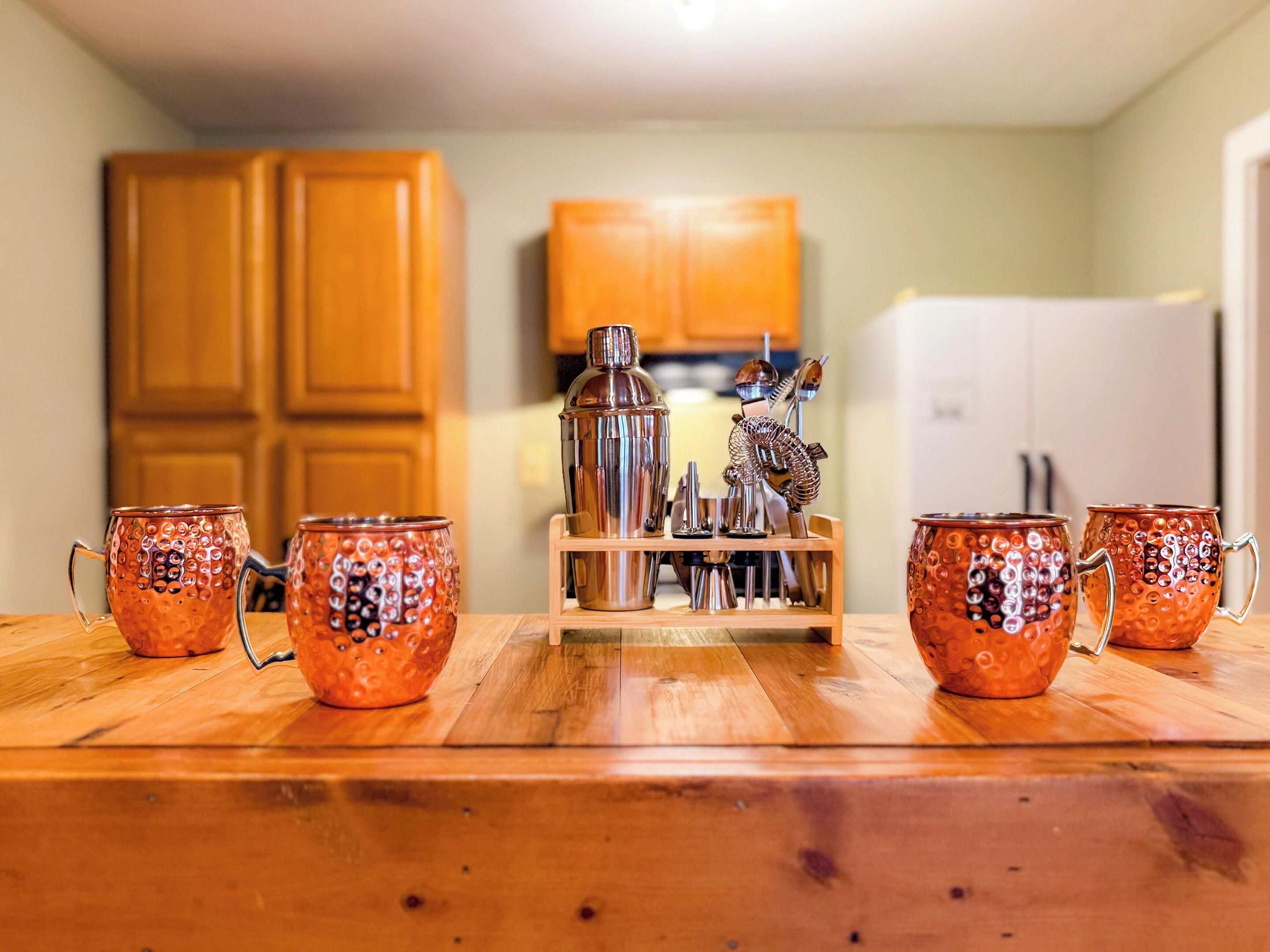 A kitchen with wooden cabinets, a stainless steel blender, and four copper mugs on a wooden table.