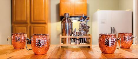 A kitchen with wooden cabinets, a stainless steel blender, and four copper mugs on a wooden table.
