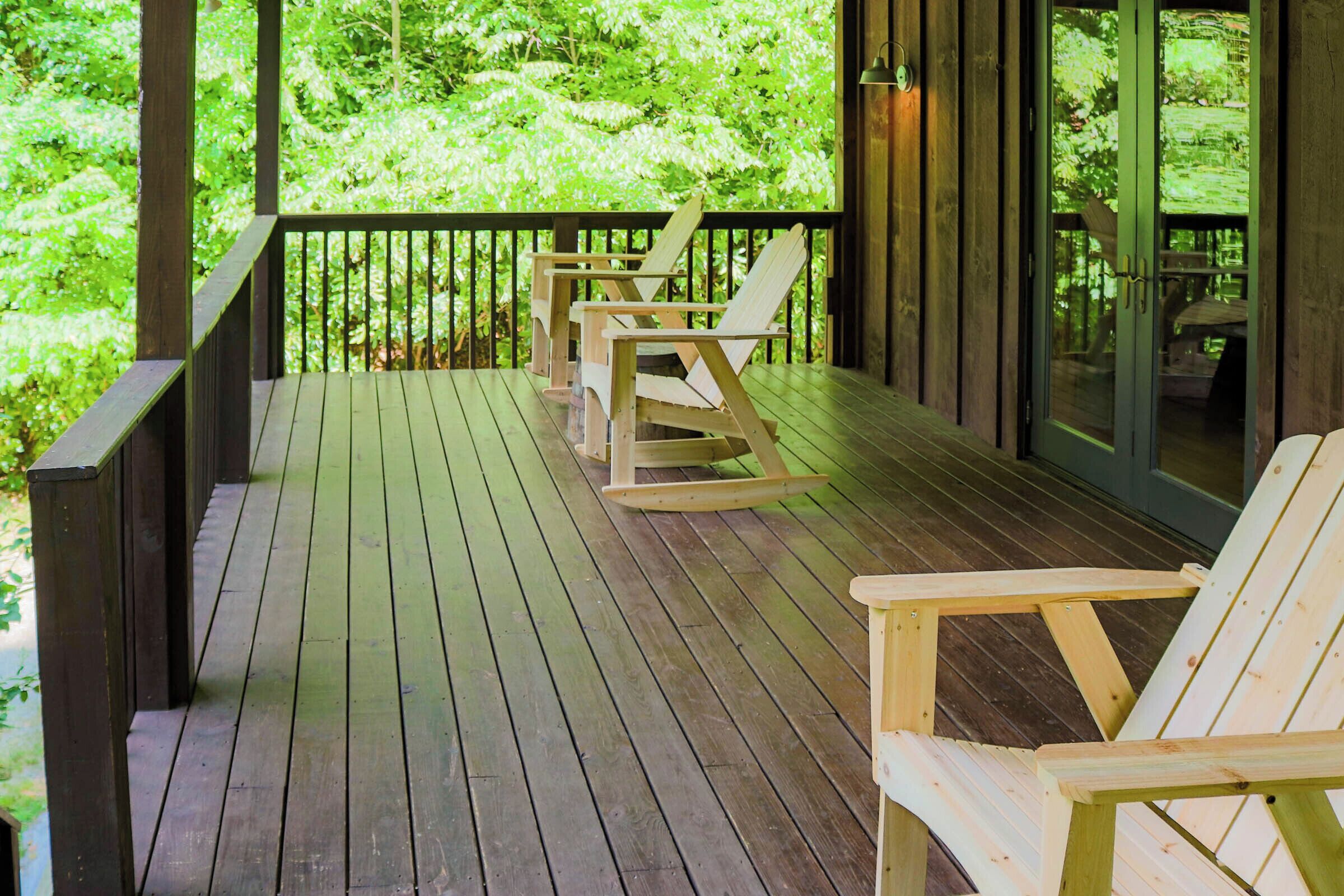 A wooden deck with rocking chairs and a glass door leading to a forested area.