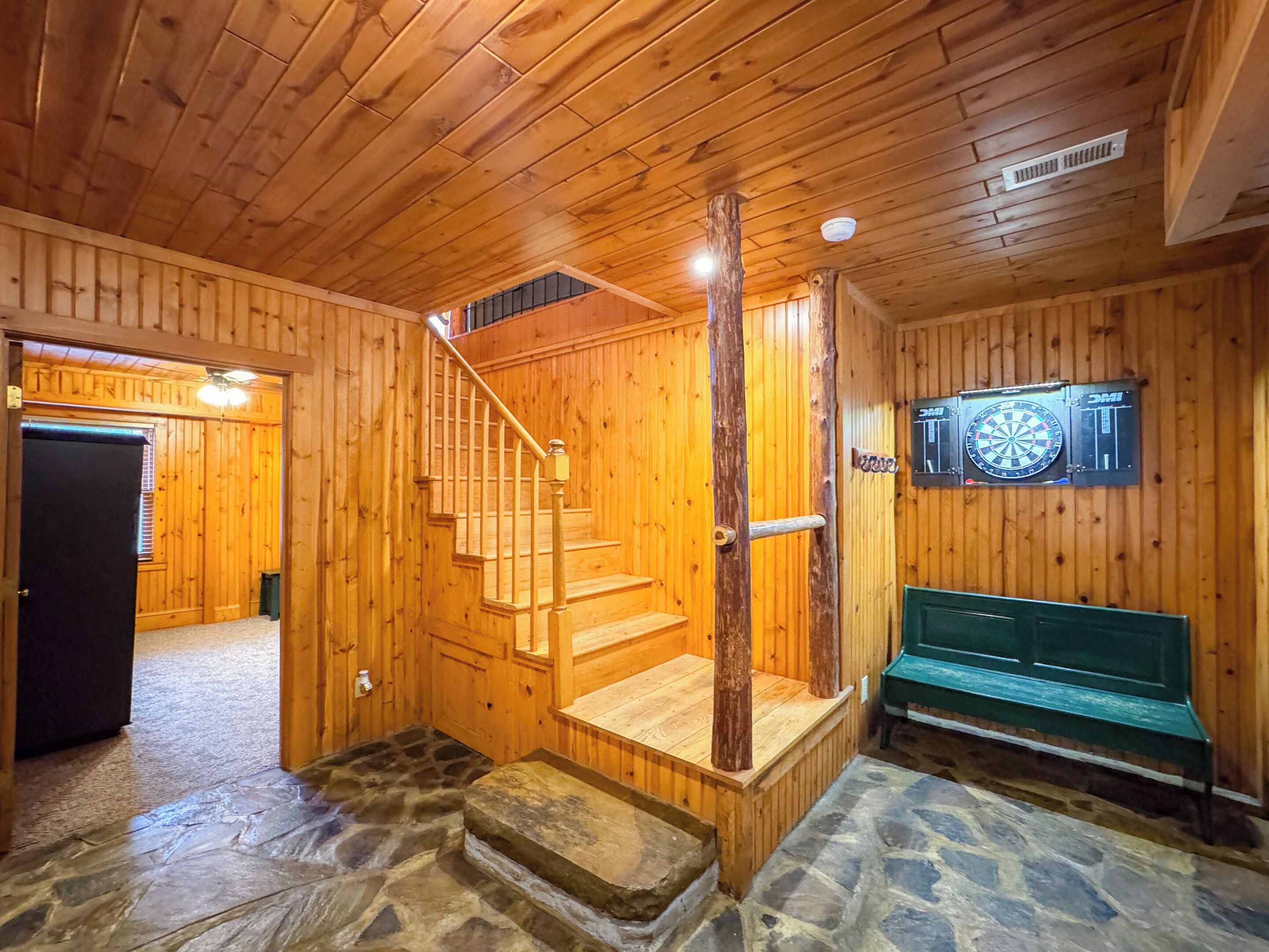 Un interior de madera con una escalera, suelo de piedra y un dardo en la pared.