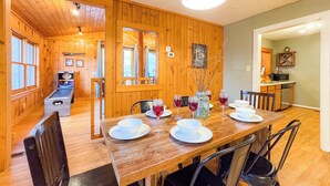 Ein Holzinterieur mit einem für vier Personen gedeckten Esstisch, einer Jukebox und einem durch eine offene Tür einsehbaren Küchenbereich.