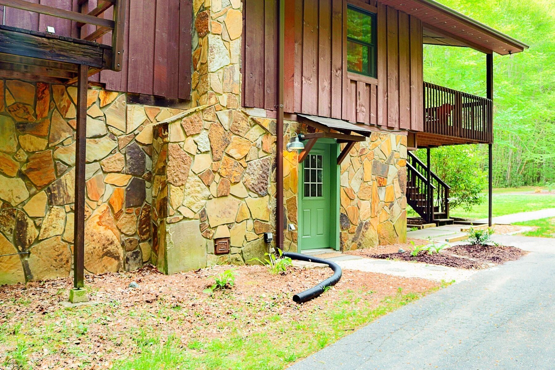 A rustic stone building with a green door, wooden porch, and a staircase leading to a balcony.