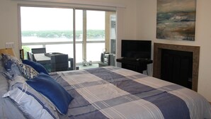 Ein Schlafzimmer mit einem großen Bett, einem Fernseher, einem Kamin und Seeblick durch eine Schiebetür.