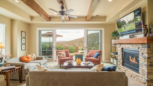 A spacious living room with a fireplace, comfortable seating, and a large TV screen displaying a golf tournament. - Sun-e-Scape- Relax in the Desert! (Washington)