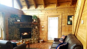 A cozy cabin interior with a stone fireplace, wooden walls, a leather sofa, and a dining area. - Enjoy Secluded Mountain Paradise at the Rustic Fox! (Sevierville)