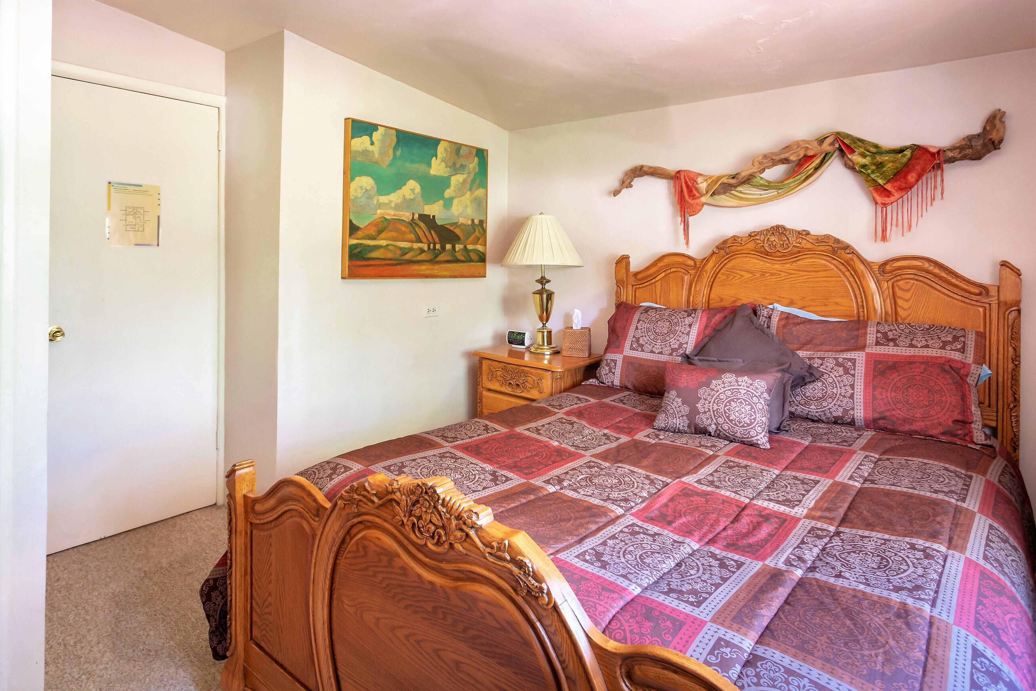 A bedroom with a wooden bed, a nightstand, a lamp, a painting, and a decorative branch on the wall.