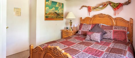 A bedroom with a wooden bed, a nightstand, a lamp, a painting, and a decorative branch on the wall.