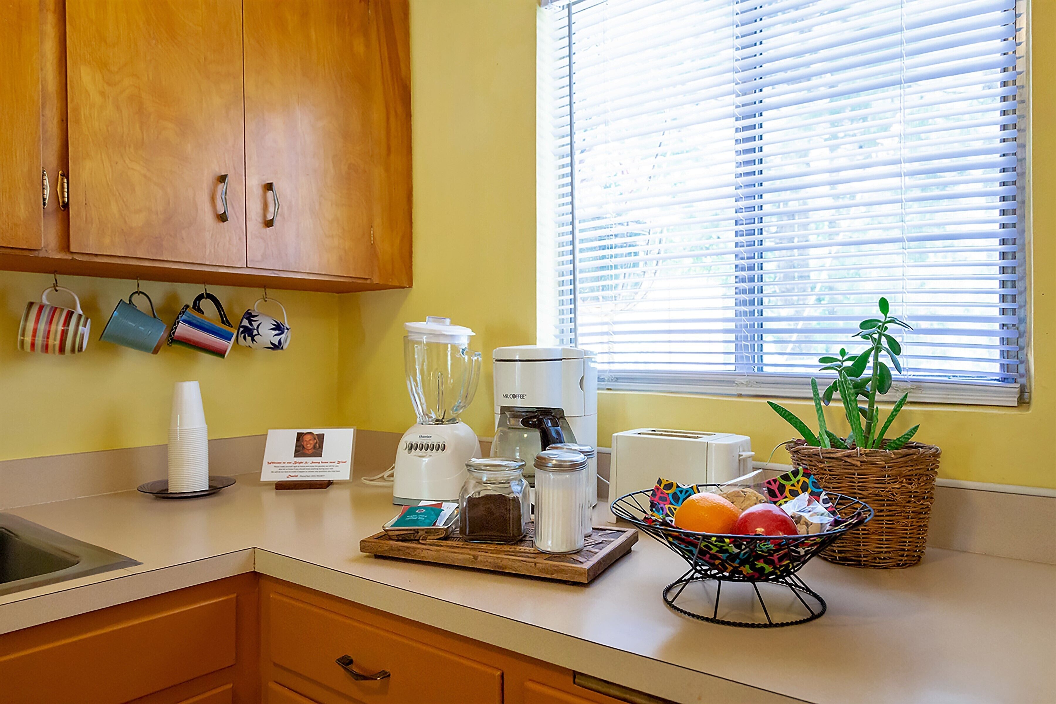 A kitchen with wooden cabinets, a coffee maker, a blender, and a fruit basket.