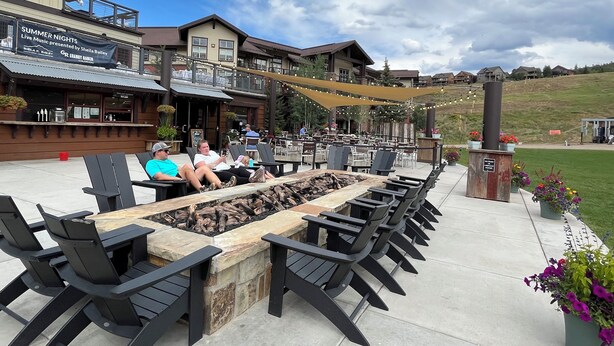 Un espace extérieur aménagé avec des fauteuils confortables et un foyer, un restaurant doté d’une terrasse, et une vue sur un paysage vallonné.