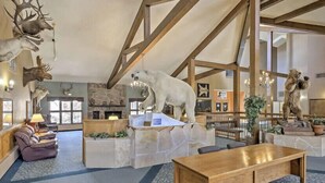 Un hall d’entrée agrémenté d’une cheminée en pierre, de canapés en cuir, d’une table en bois et de diverses pièces de taxidermie représentant des animaux.