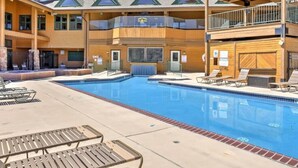 Un immeuble à plusieurs étages doté d’un espace piscine, comprenant des chaises longues et une piscine à l’eau d’un bleu cristallin.