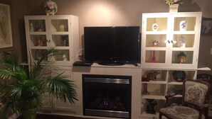 A living room with a television, cabinets with glass doors, a fireplace, and a chair.
