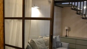 Een kamer met een schuifglaswand, een bed met kussens, een nachtkastje met een lamp en een visgraatvloer.