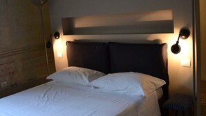 Een hotelkamer met een groot bed, twee bedlampen en een bankje bij het raam.