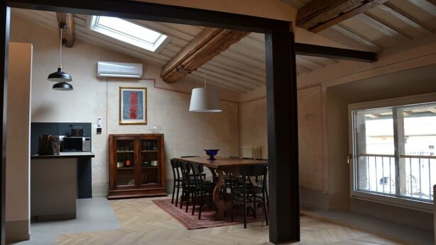 Een eetgedeelte met een houten tafel en stoelen, een keuken met een magnetron en kasten, en een groot raam met uitzicht.