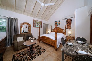 A hotel room with a bed, a sofa, a dining table, and a ceiling fan.