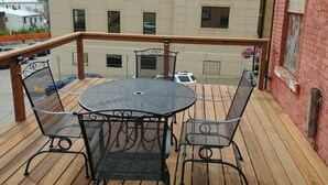 A wooden deck with a round table and four chairs, overlooking a building with a sign reading "Decorah Public Library".