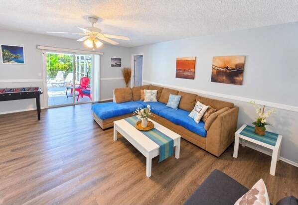 A living room with a sectional sofa, a coffee table, a side table, and a ceiling fan.