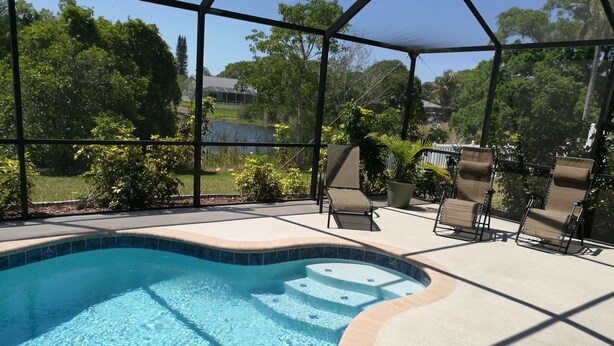 A swimming pool with a curved edge, surrounded by a covered patio area with chairs and a sunshade. - 3/2 Home Heated Pool / close to Beautiful Anna Maria Beaches / close to IMG (Bradenton)