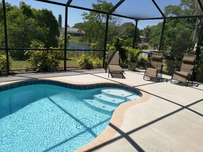A swimming pool with a curved edge, surrounded by a covered patio area with chairs and a sunshade.
