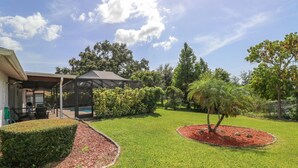 A well-maintained garden with a covered patio, a swimming pool, and various trees and shrubs. - 3/2 Home Heated Pool / close to Beautiful Anna Maria Beaches / close to IMG (Bradenton)