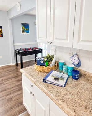 A kitchen with white cabinets, a foosball table, and a basket containing a bottle and a plant.