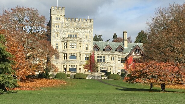 A large stone building with a flag, surrounded by a well-maintained lawn and autumn-colored trees.