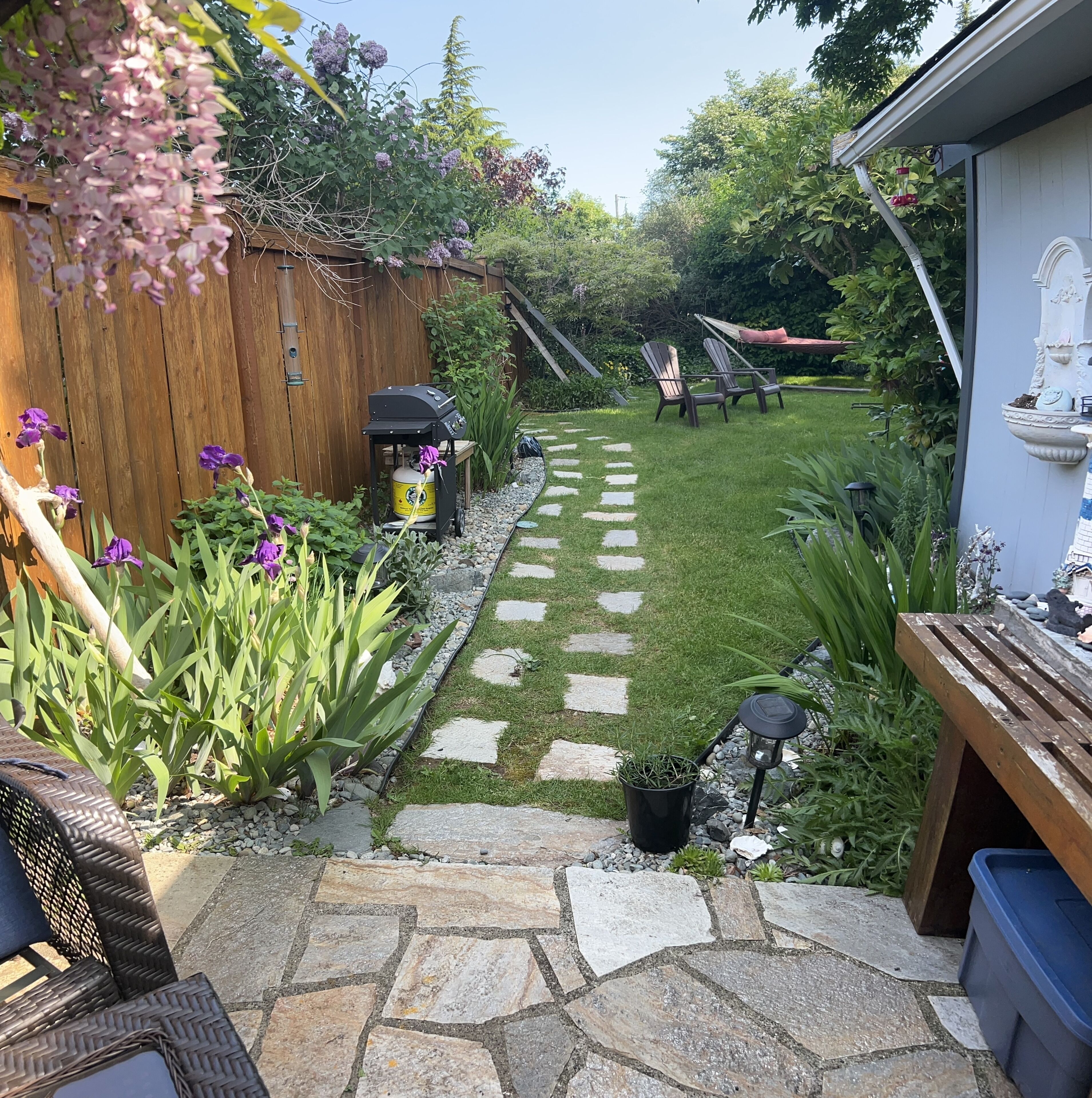 A stone pathway leading to a backyard with a wooden fence, a grill, and outdoor seating.