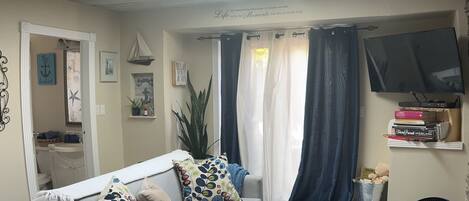 Una sala de estar con un sofá gris, una mesa de centro, un televisor y un ventilador.