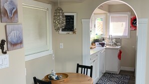 A dining area with a wooden table and chairs, a blue patterned rug, and a kitchen visible through an archway.