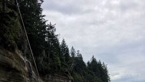 A person swinging on a rope over a beach with a rocky cliff and ocean in the background.