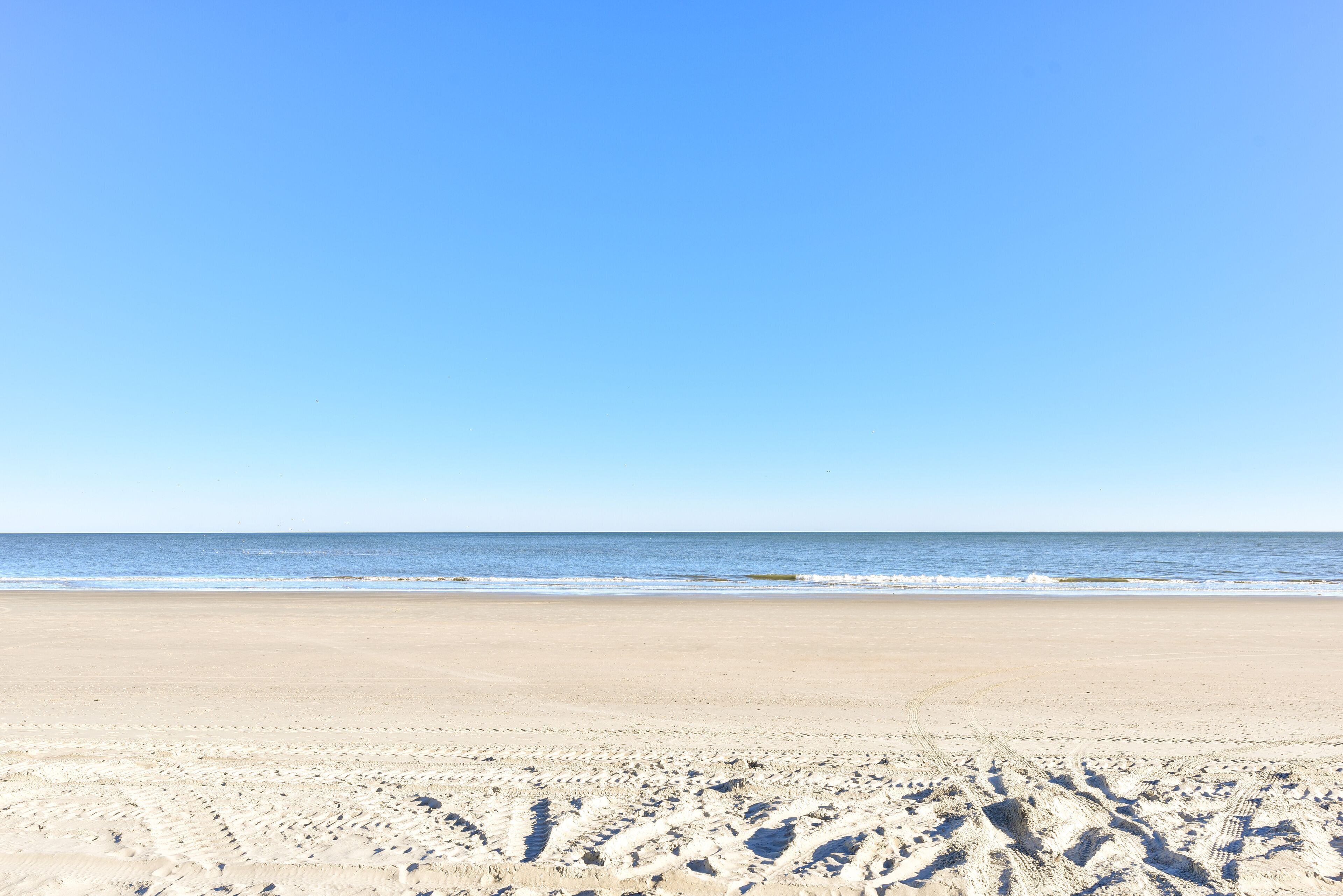 A beach with footprints in the sand and a clear blue sky.