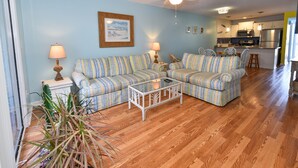 A living room with striped sofas, a coffee table, and a dining area with chairs. - Fully Remodeled Bright and Beautiful  2bed 2 bath condo just steps to the Beach (Murrells Inlet)