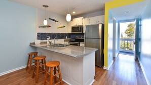 A kitchen with a central island, wooden stools, a microwave, and a refrigerator. - Fully Remodeled Bright and Beautiful  2bed 2 bath condo just steps to the Beach (Murrells Inlet)