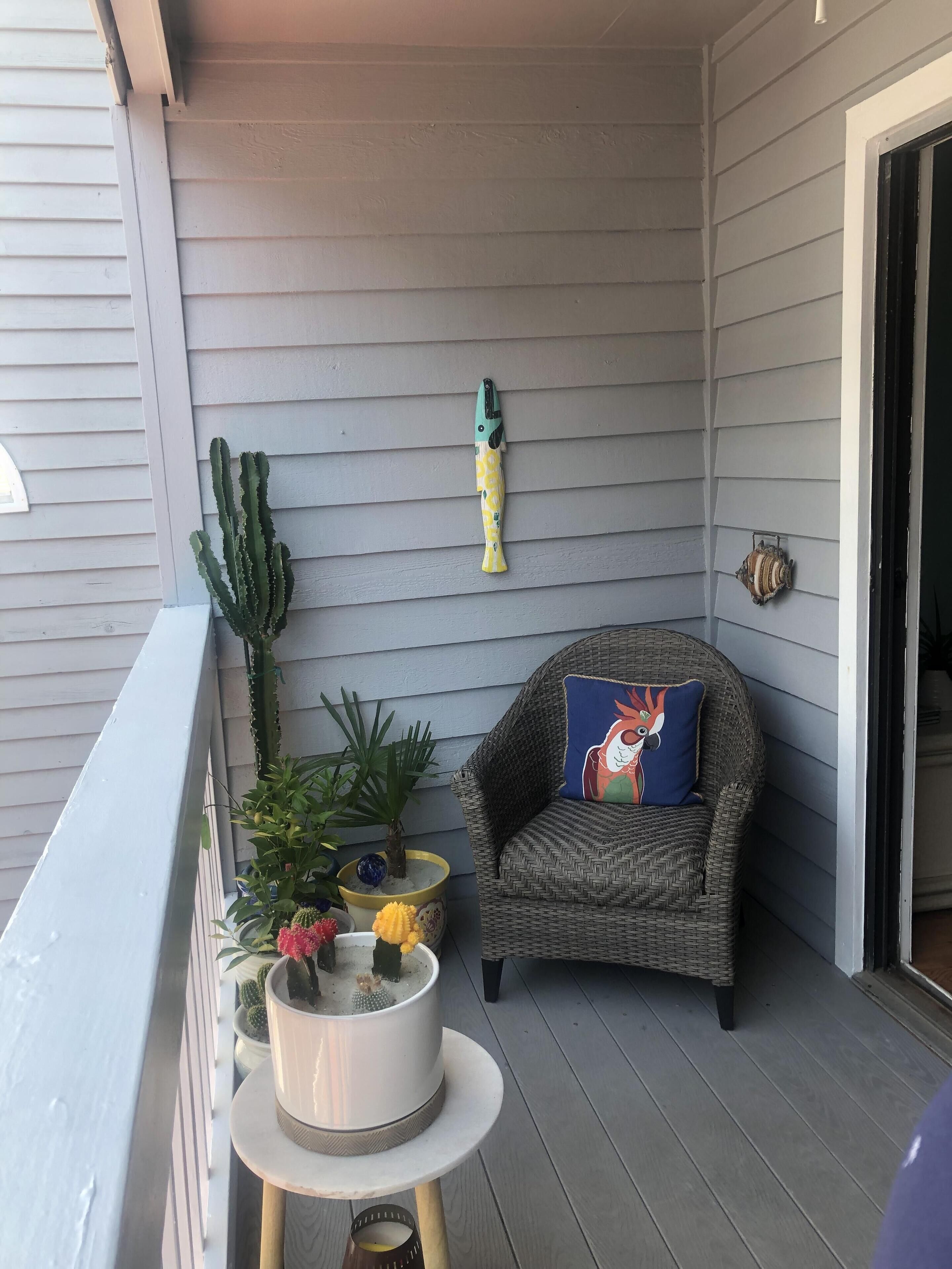 A balcony with a wicker chair, a cactus, and a small table with a decorative item.