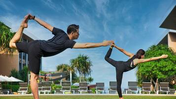 Two people practicing yoga outdoors with a pool and lounge chairs in the background.