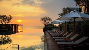 Vista del atardecer desde una terraza con sillones reclinables y sombrillas, con vista a una masa de agua tranquila.