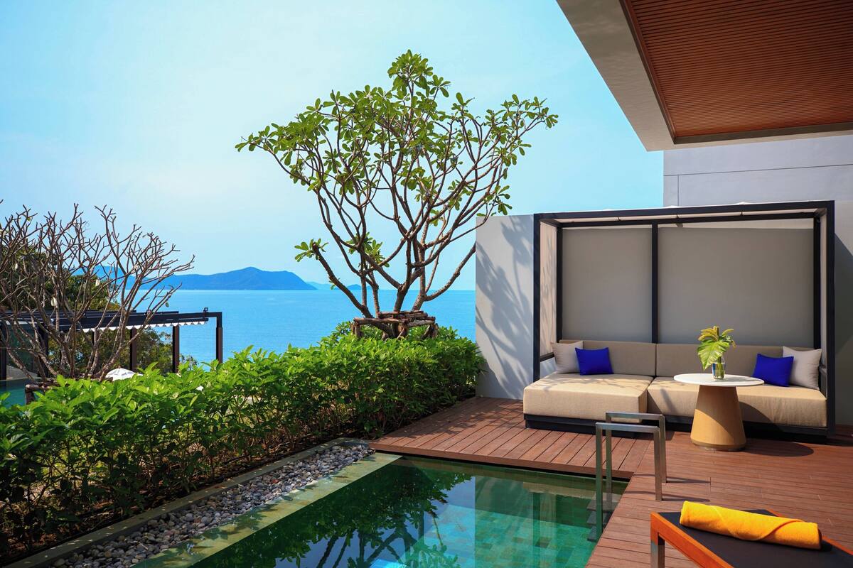A modern outdoor lounge area with a pool, wooden deck, and a sofa with cushions.