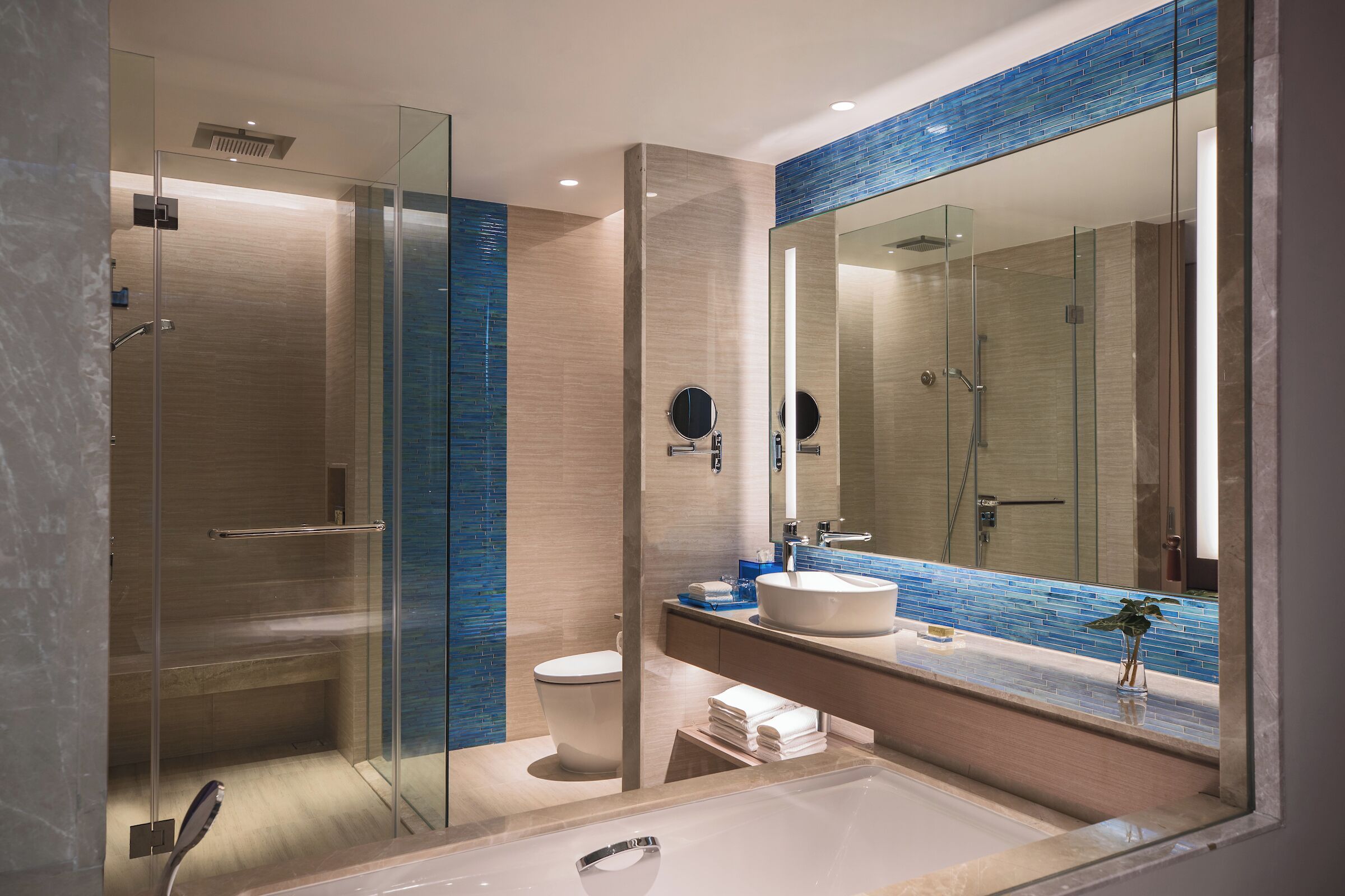 A modern bathroom with a glass-enclosed shower, a large mirror, and a sink with a blue-tiled backsplash.